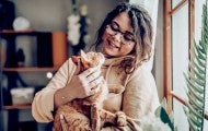 A woman holds a cat in her arms as they look lovingly at each other
