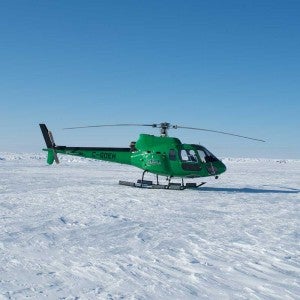a green helicopter landed on flat, snow-covered land