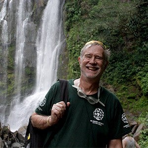 A smiling man stands in front of a waterfall
