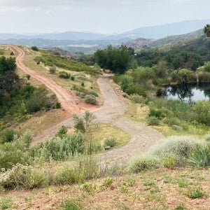 A dirt and gravel road on a hillside with water and low mountains in the background