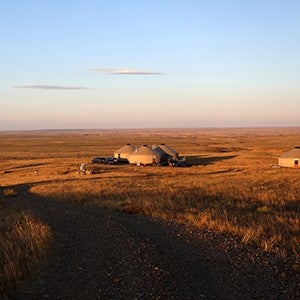 Wide view of an expansive prairie with yurt structures in the distance