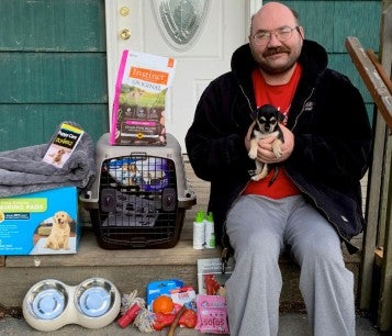 Man sitting with his new puppy sitting on his porch filled with pet supplies