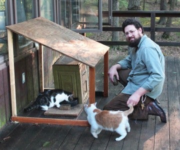Jim O'Hagan sitting with colony cats at feeding station