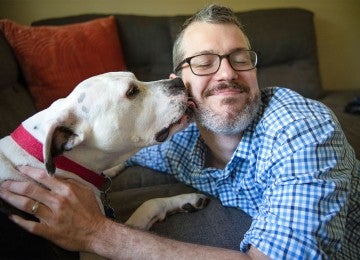A man getting a kiss from a white dog