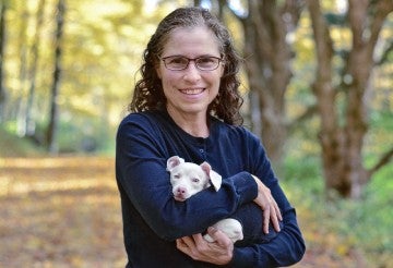A woman holds a small, white dog in her arms and smiles.