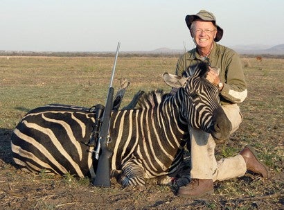 A trophy hunter props up the head of a zebra he killed for the obligatory photo.