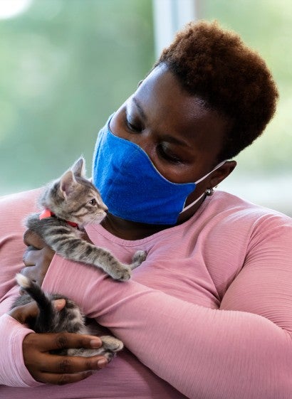 A woman wearing a mask and holding a kitten