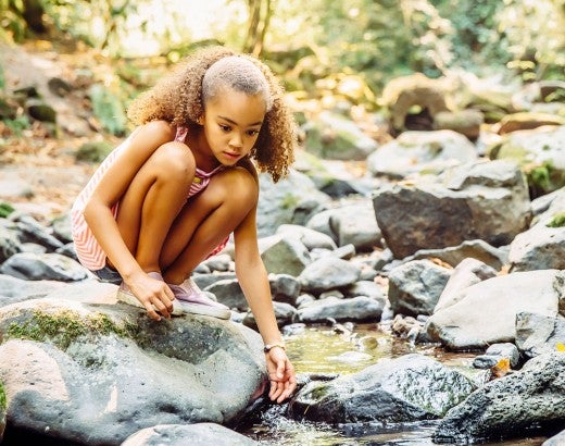 Young girl playing near stream in forest
