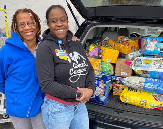 Two women standing in front of their car trunk full of pet food donations