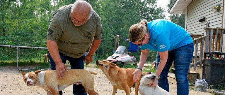 Rick Haaland of Leech Lake Band of Ojibwe Pets for Life and Rachel Thompson from Pets for Life pet three dogs outside a home