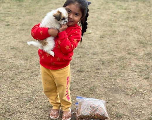 A young girl holds her puppy next to a bag of free food given by Pets for Life during their response to the COVID-19 pandemic in Granger, Washington